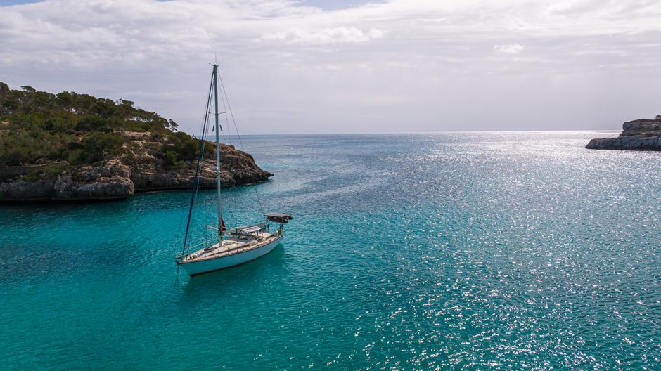 A tranquil scene of a sailboat anchored in a beautiful cove in Mallorca, Spain, with clear blue waters.