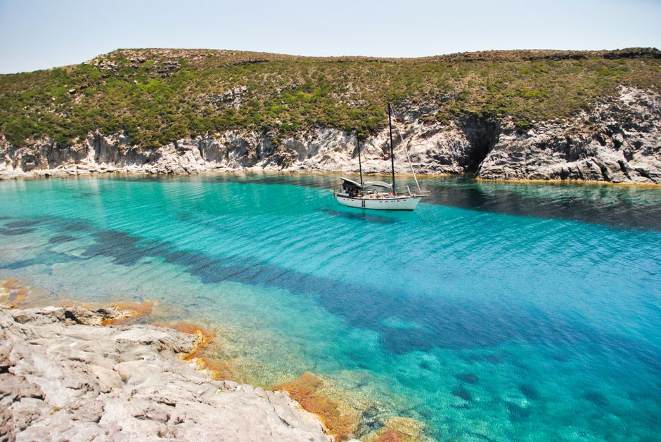 A tranquil sailboat floats on clear blue waters near rocky Sardinian coastline.