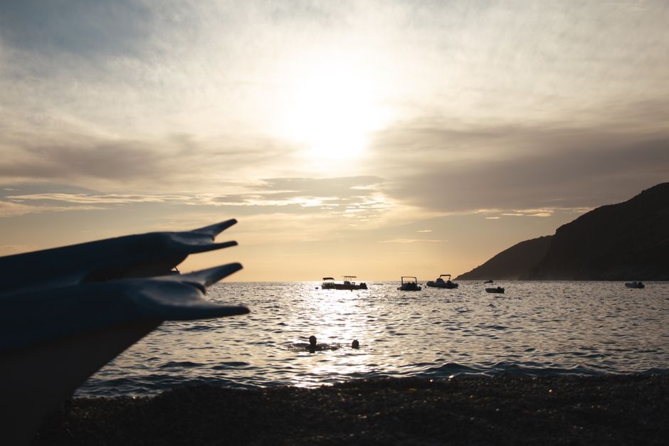 A peaceful sunset at a beach in Vlorë County, Albania with boats and swimmers in the sea.